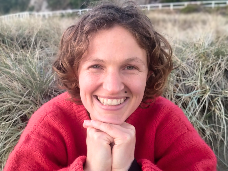 Woman sitting amongst coastal bush smiling