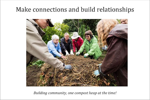 A group of people gathered around a compost heap with their hands stretched out, touching the compost